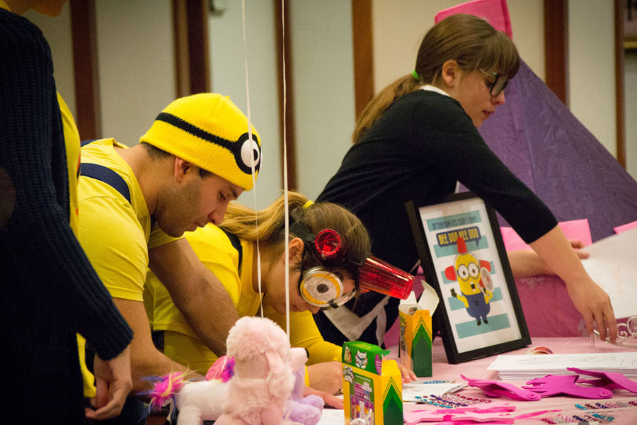 Students, dressed as Minions, color with children at a table