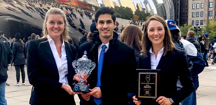 A Baylor Law moot court team holding trophies in front of Chicago's Bean sculpture 