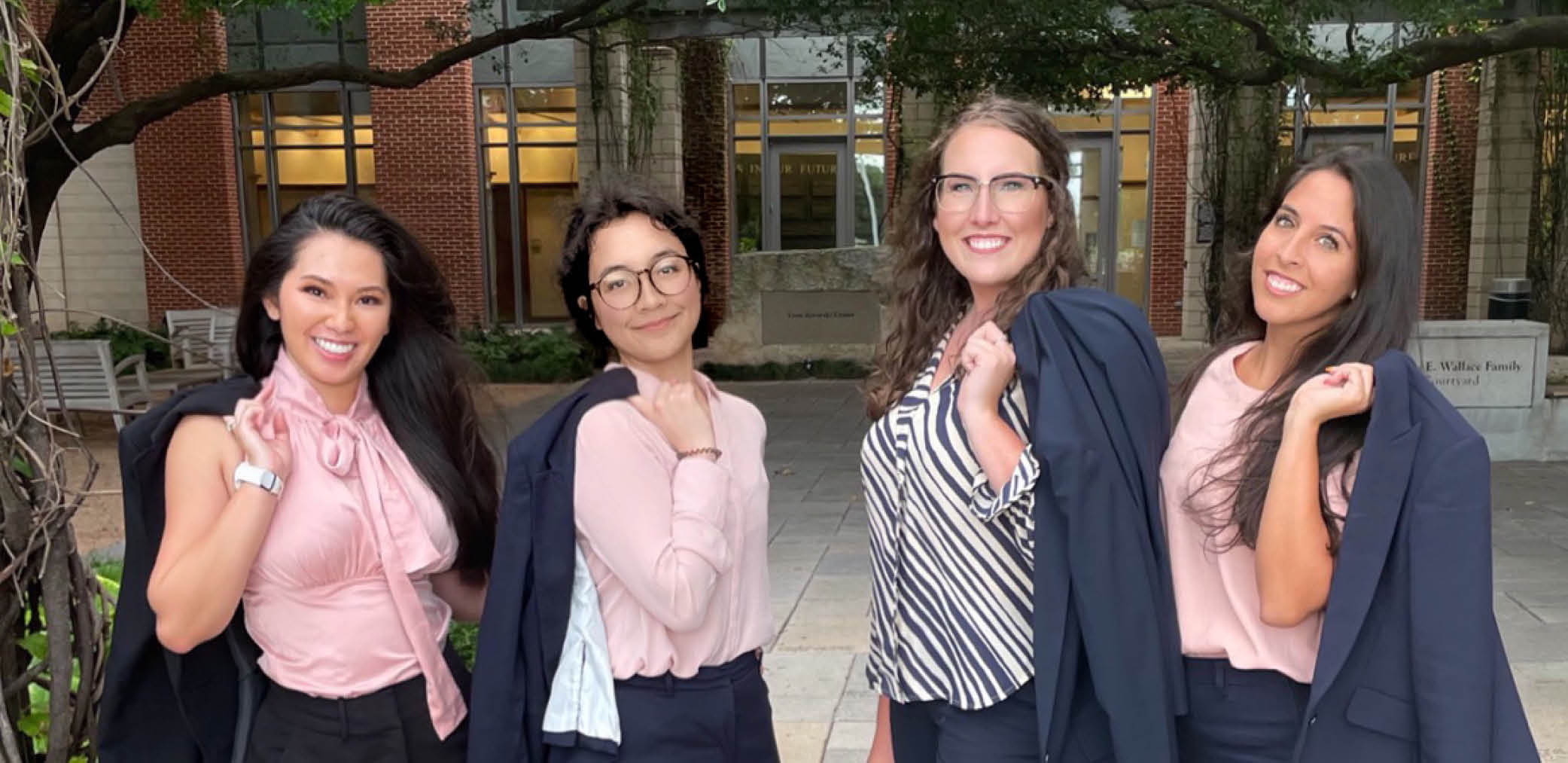 Four Baylor Law students, with jackets flung over their shoulders, pose in front of the law center