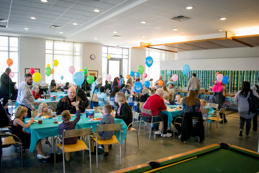 Photo of Law School Cafe decorated for Adoption Day. Tables are full of families eating, colorful balloons are everywhere.