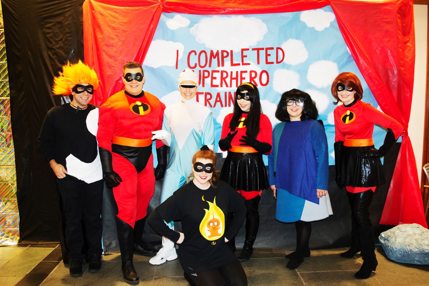 Baylor Law faculty, staff and students dressed as characters from Disney's "The Incredibles" pose in front of banner that reads, "I Completed Superhero Training."
