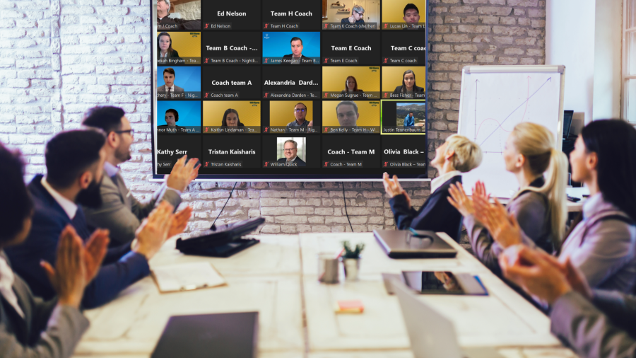 Several people in conference room clapping at The Closer Competition that is being broadcast on TV on the wall