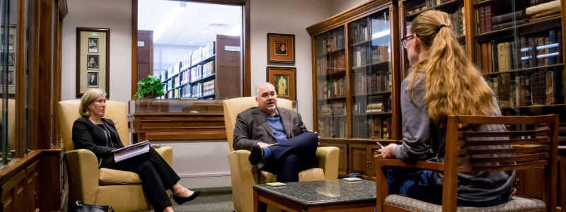 Law school student interviews clients, surrounded by law library books